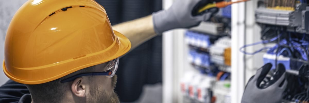 A male electrician works in a switchboard with an electrical connecting cable.